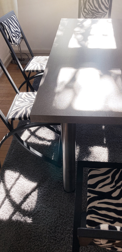 Ausschnitt eines grauen Tisches umrahmt von vier Stühlen mit Zebra-Muster in stimmungsvollem Licht